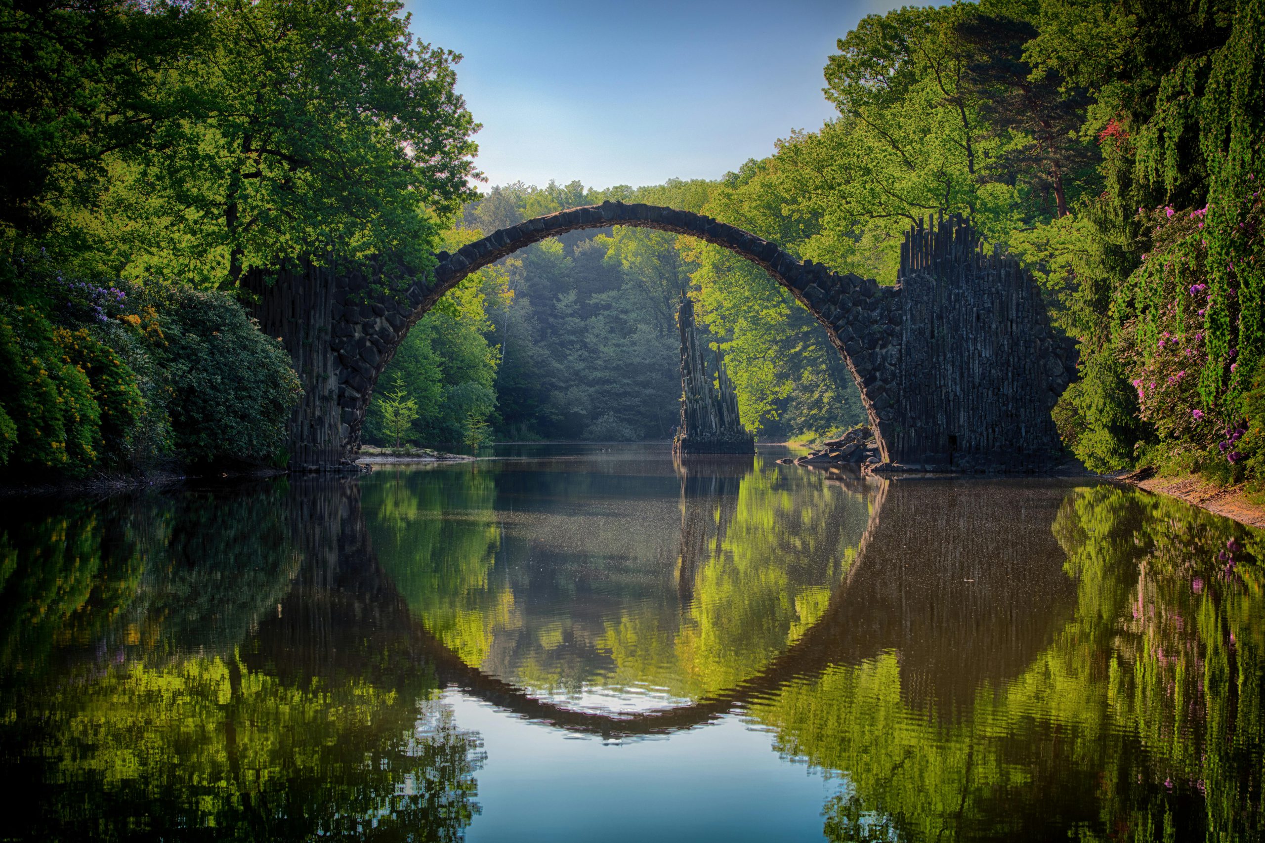 Capture of the iconic Rakotzbrücke reflecting in calm waters amidst lush greenery in Germany.
